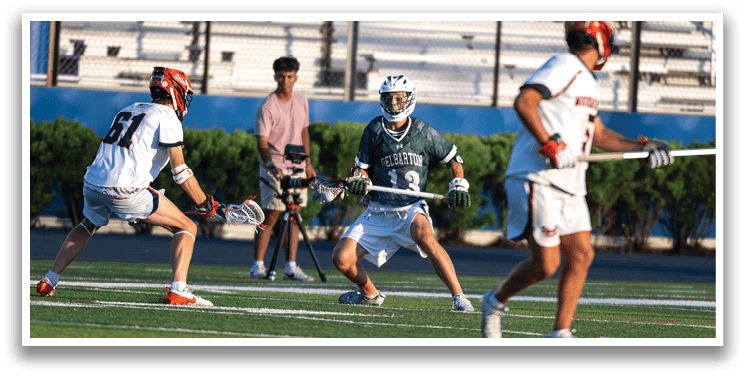 Two men playing lacrosse on a field. Description generated by AI