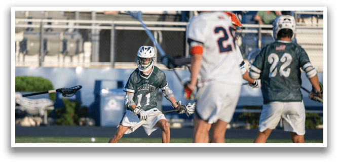 A man in a green shirt is holding a lacrosse stick. Description generated by AI