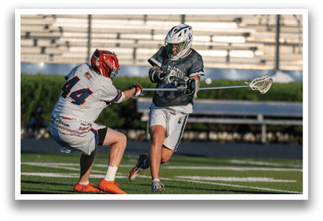 A man in a green and white uniform is holding a stick and running on a field. Description generated by AI