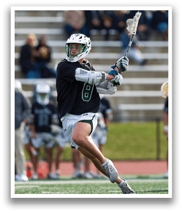 A man wearing a black shirt and green shorts is holding a lacrosse stick. Description generated by AI
