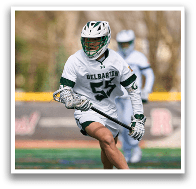 A man wearing a white and green shirt and white shorts is holding a stick and running on a field. Description generated by AI