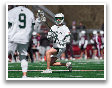 A man in a white jersey is holding a lacrosse stick. Description generated by AI