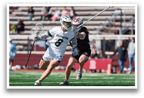 A man in a white shirt and green shorts is running with a lacrosse stick. Description generated by AI