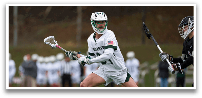A man in a white uniform is holding a lacrosse stick and running on a field. Description generated by AI