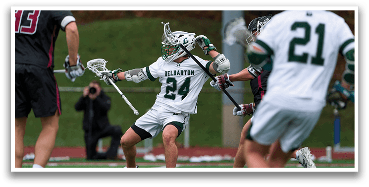 A man in a green and white uniform is holding a lacrosse stick. Description generated by AI