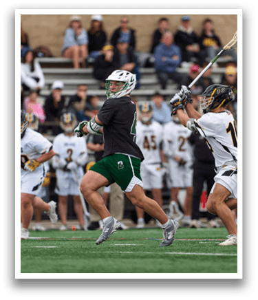 A man in a green and white uniform is running with a lacrosse stick. Description generated by AI