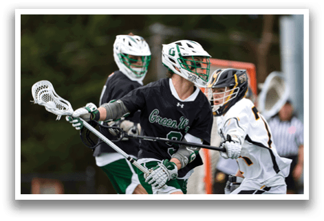 A man wearing a black shirt and green shorts holding a lacrosse stick. Description generated by AI