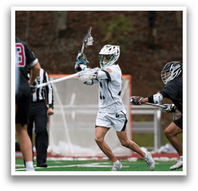 A man in a white shirt and green shorts is holding a lacrosse stick. Description generated by AI