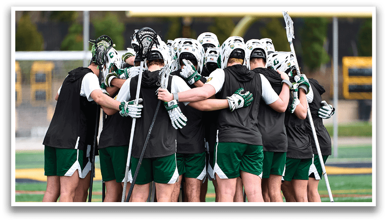 A group of people wearing green and white huddled together on a field. Description generated by AI