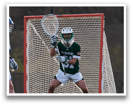 A man in a green shirt and white shorts is playing lacrosse. Description generated by AI