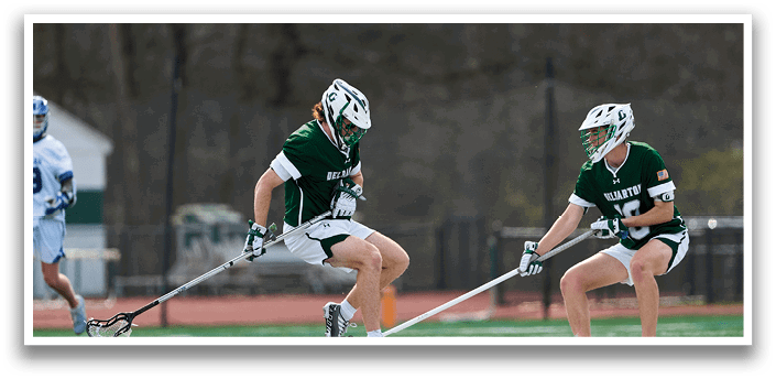 Two men playing a game of lacrosse on a field. Description generated by AI
