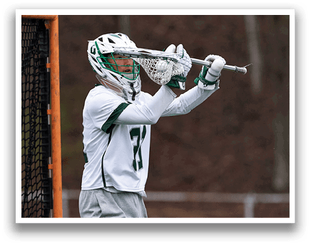A man wearing a green and white uniform is holding a lacrosse stick. Description generated by AI