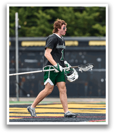 A man wearing a black and green shirt and shorts holding a lacrosse stick. Description generated by AI