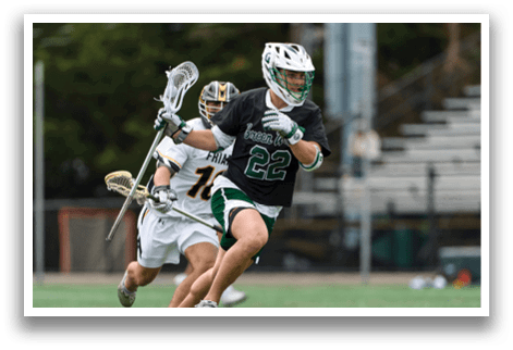 A man in a black shirt and green shorts is running on a field with a lacrosse stick. Description generated by AI