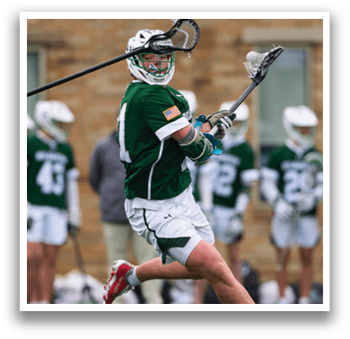 A man wearing a green shirt and white shorts is holding a lacrosse stick. Description generated by AI