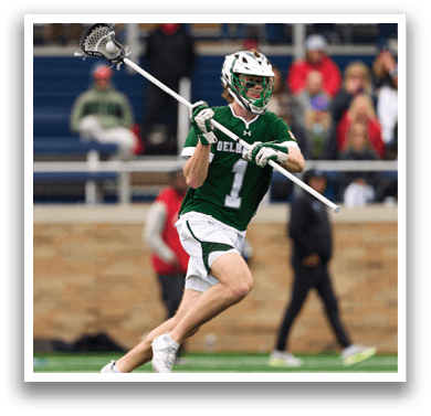 A man wearing a green and white uniform is running with a lacrosse stick. Description generated by AI