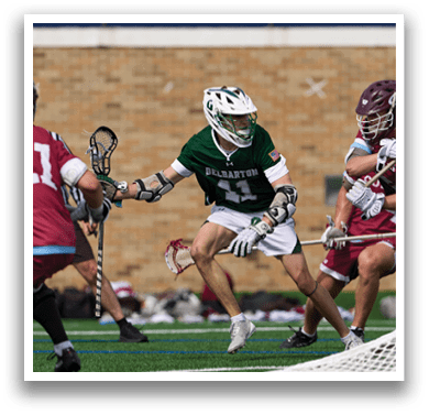 A man in a green shirt and white shorts is holding a lacrosse stick. Description generated by AI