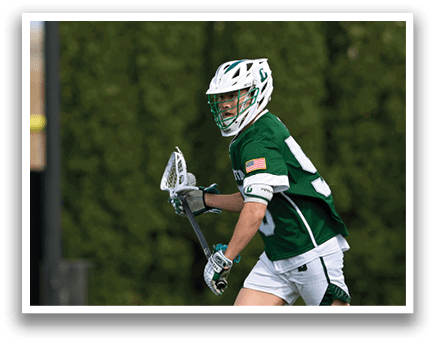 A man wearing a green and white uniform is holding a lacrosse stick. Description generated by AI