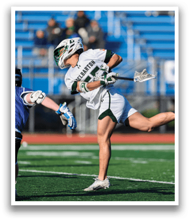 A man wearing a white and green shirt is holding a lacrosse stick. Description generated by AI