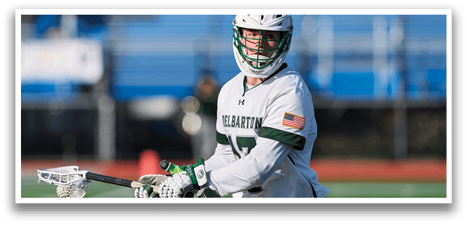 A man in a white and green uniform holding a lacrosse stick. Description generated by AI