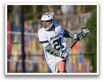 A man in a white and green uniform is holding a lacrosse stick. Description generated by AI