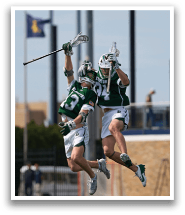 Two men jumping in the air with their lacrosse sticks. Description generated by AI