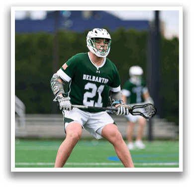 A man wearing a green shirt and white shorts holding a lacrosse stick. Description generated by AI
