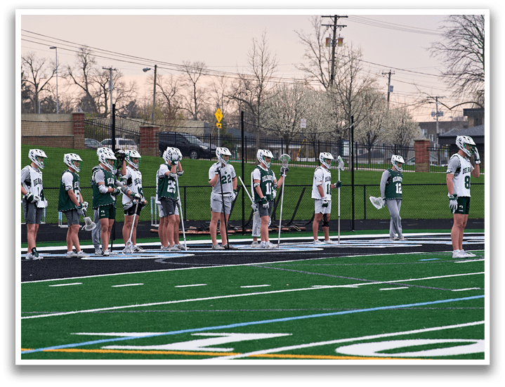 A group of people wearing green and white uniforms and holding lacrosse sticks. Description generated by AI