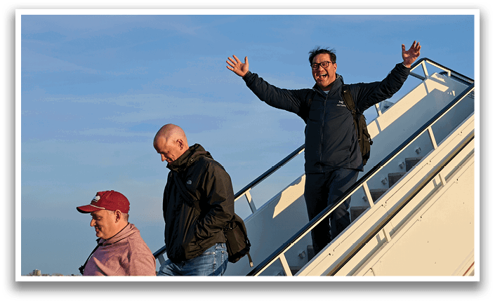 Three men are getting off an airplane. Description generated by AI