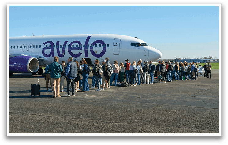 A large group of people are standing on the tarmac in front of a white and purple airplane. Description generated by AI