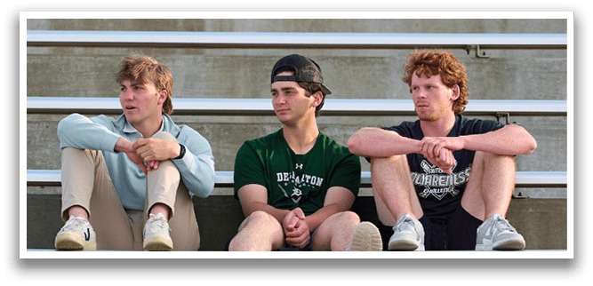 Three boys sitting on bleachers. Description generated by AI