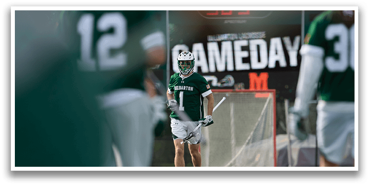 A man in a green and white uniform is holding a hockey stick. Description generated by AI