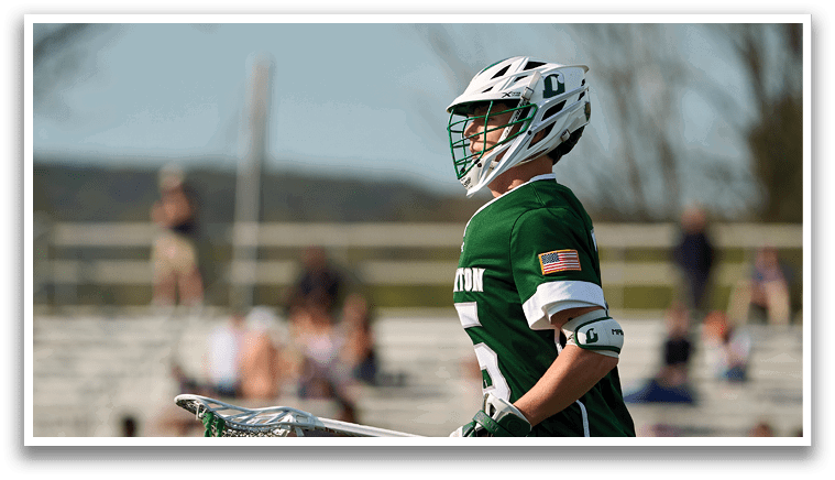 A man wearing a green and white uniform holding a lacrosse stick. Description generated by AI