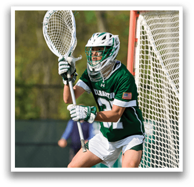 A man wearing a green and white uniform is holding a lacrosse stick. Description generated by AI