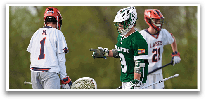 A man wearing a green shirt and white shorts holding a lacrosse stick. Description generated by AI