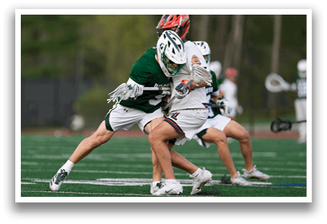 Two men playing lacrosse on a field. Description generated by AI