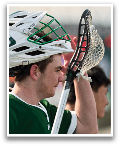 A man wearing a green shirt and white helmet holding a lacrosse stick. Description generated by AI