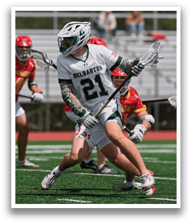 A man wearing a green and white uniform is holding a lacrosse stick. Description generated by AI