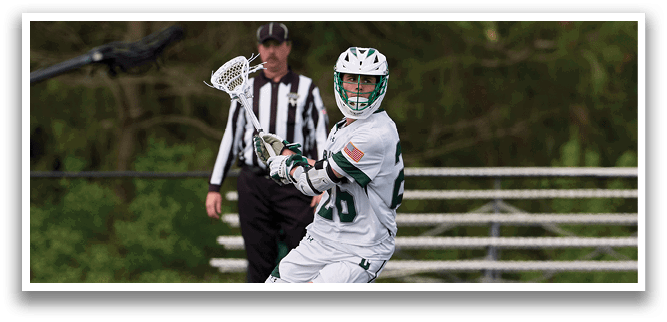A man in a white shirt and green shorts is holding a lacrosse stick. Description generated by AI