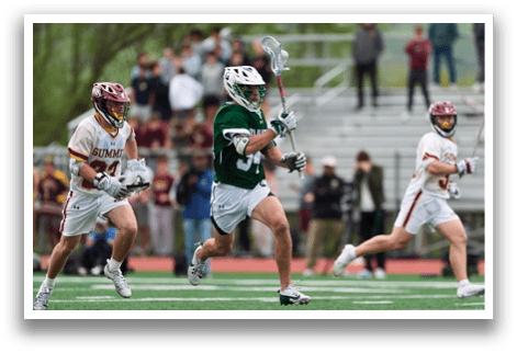 A man in a green shirt and white shorts is holding a lacrosse stick. Description generated by AI