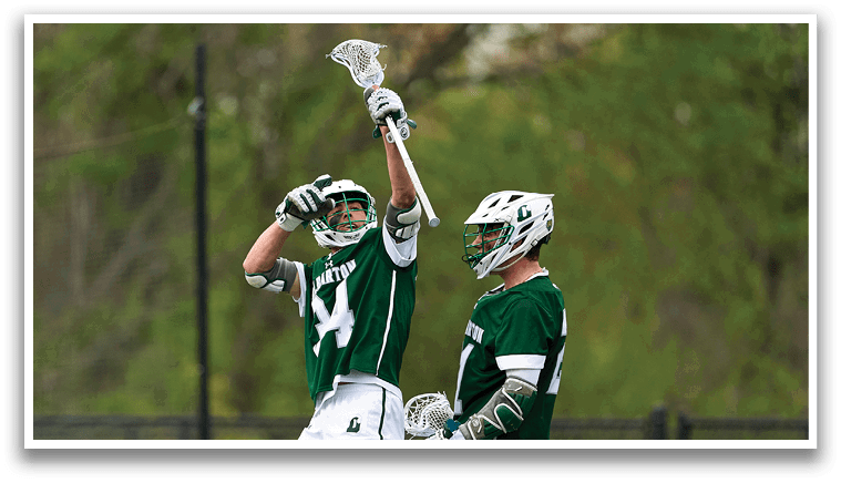Two men wearing green and white uniforms are holding their lacrosse sticks in the air. Description generated by AI