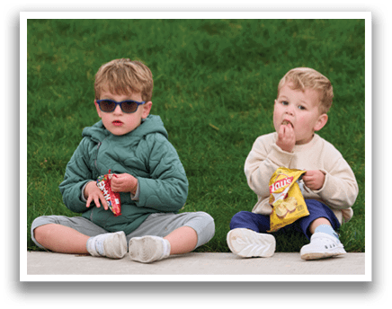 Two young boys sitting on the ground eating chips and soda. Description generated by AI