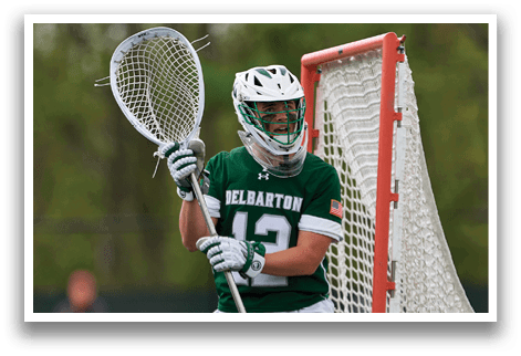 A man wearing a green and white uniform is holding a lacrosse stick. Description generated by AI