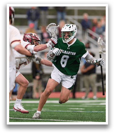 A man wearing a green shirt and white shorts is running with a lacrosse stick. Description generated by AI