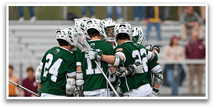A group of men wearing green and white uniforms huddle together on a field. Description generated by AI