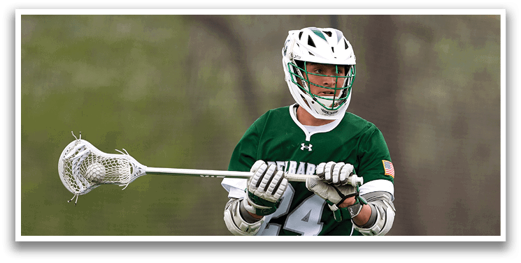 A man wearing a green shirt and white shorts is holding a lacrosse stick. Description generated by AI