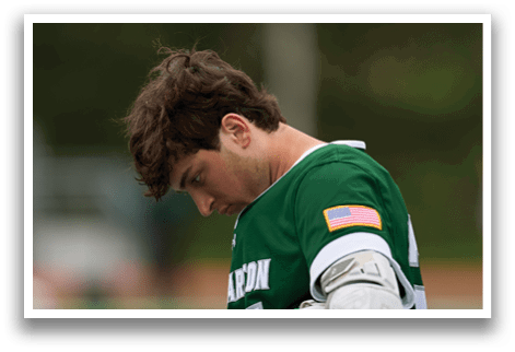 A man wearing a green and white shirt and holding a lacrosse stick. Description generated by AI