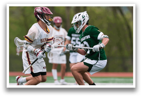 Two men playing lacrosse on a field. Description generated by AI