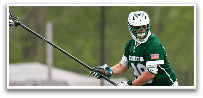 A man wearing a green shirt and white shorts holding a lacrosse stick. Description generated by AI