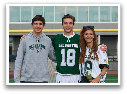 A man wearing a Delmarion jersey poses with a woman and a boy. Description generated by AI